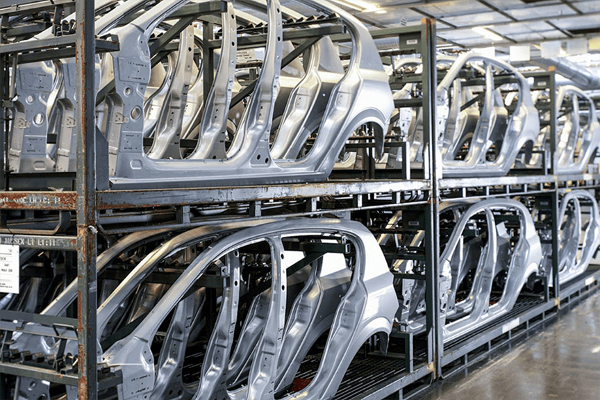 Silver car frames lined up and stacked in a warehouse ready for assembly