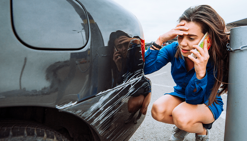 Woman looking at scratch on her black car because someone performed a Rhode Island Hit And Run